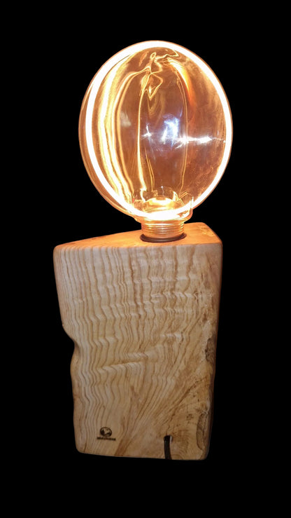 Back view of a handcrafted triangular Ash wood lamp base with a large glowing circular Edison bulb.